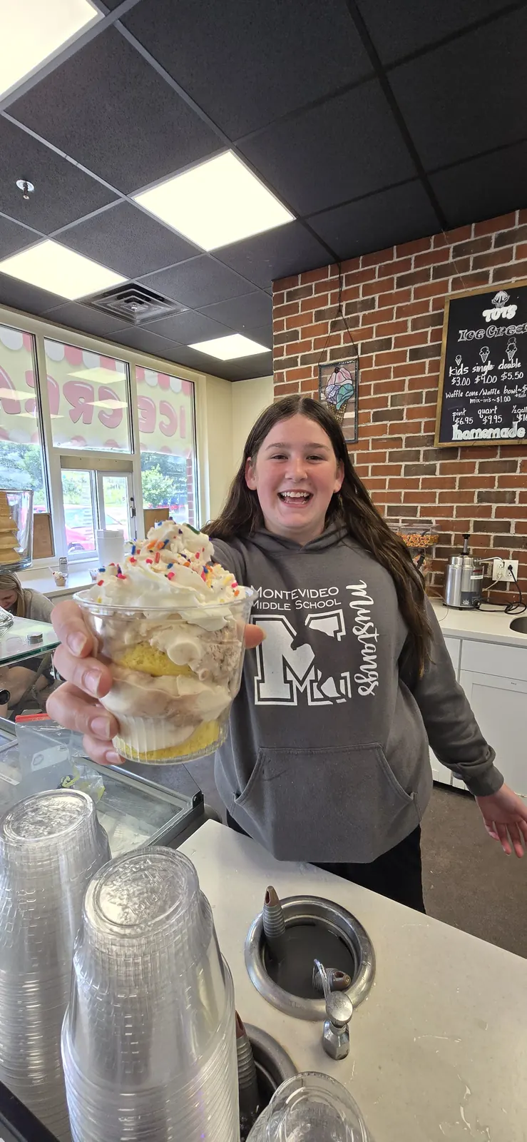Smiling customer holding a sprinkle cake sundae inside Tots Ice Cream