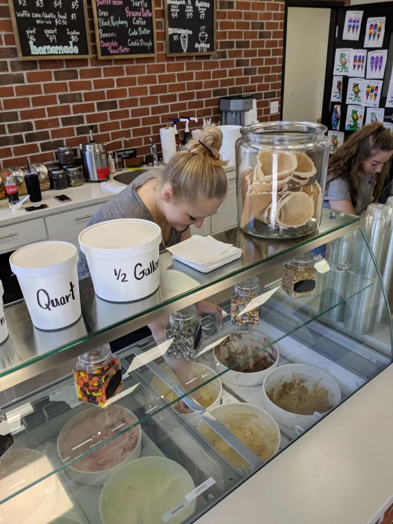 Scooping homemade ice cream from the dipping case, with quart and half gallon containers on top