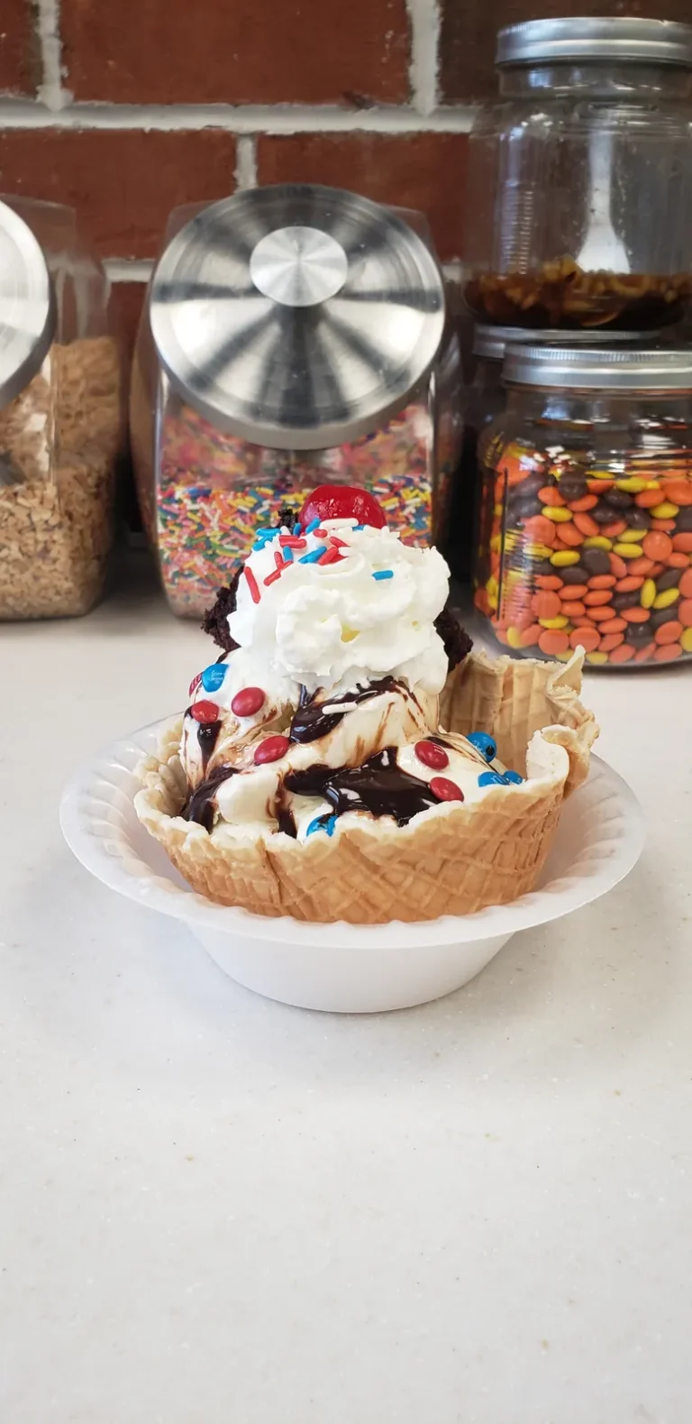 Waffle bowl sundae with M&Ms in front of jars of toppings